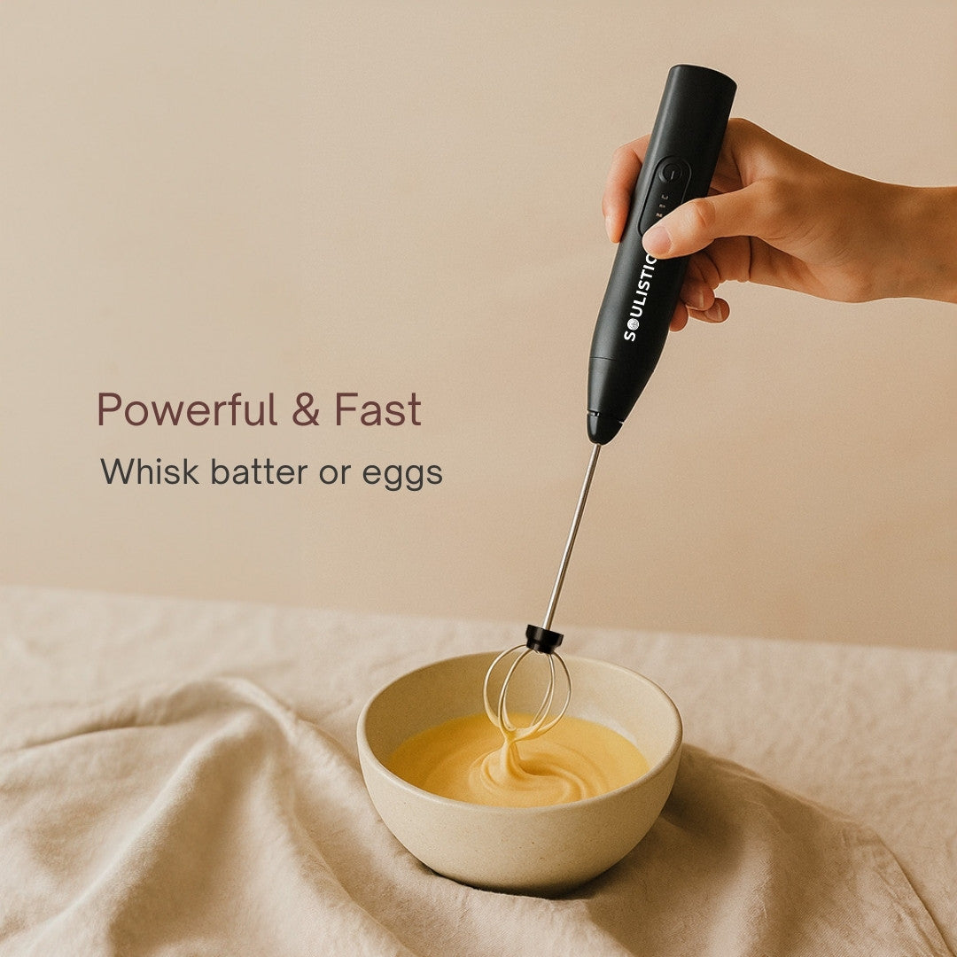Hand holding a black Electric whisker whisking batter in a white bowl on a beige background