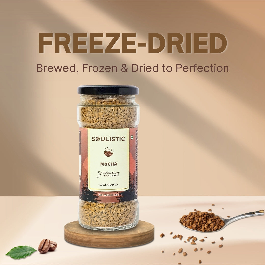 Jar of freeze-dried Soulistic mocha on a wooden coaster with a spoonful of coffee granules.