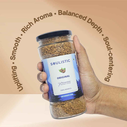 Hand holding a Soulistic Original 100% Arabica Instant Coffee jar with its qualites written around it