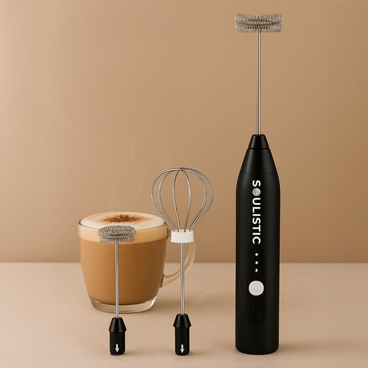 Black milk frother with whisk next to a mug of coffee on a beige background