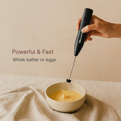 Hand holding a black Electric whisker whisking batter in a white bowl on a beige background