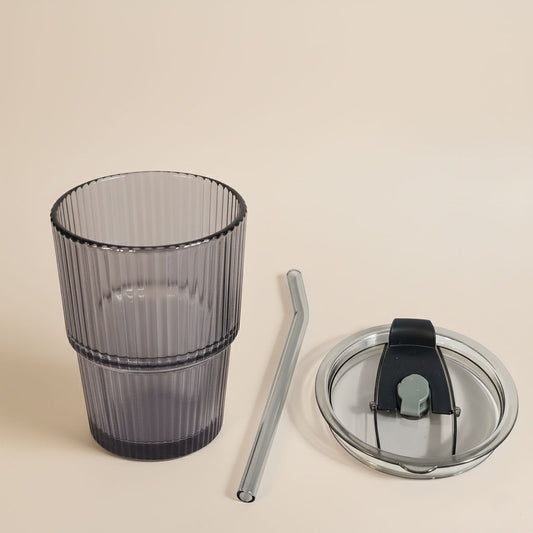 Glass tumbler with a straw and lid on a beige background
