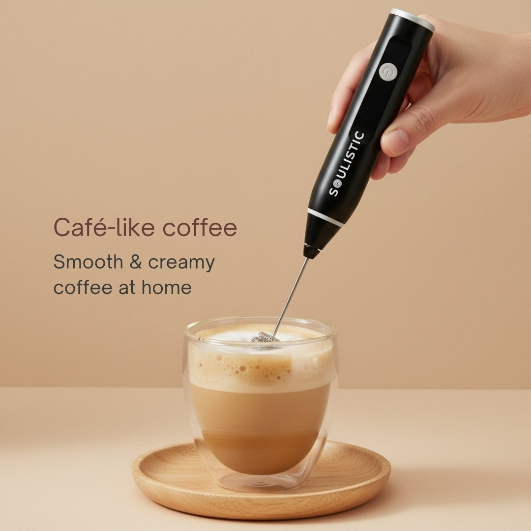 Hand using a Soulistic milk frother to create foam in a glass of coffee with text 'Café-like coffee Smooth & creamy coffee at home' on a beige background.