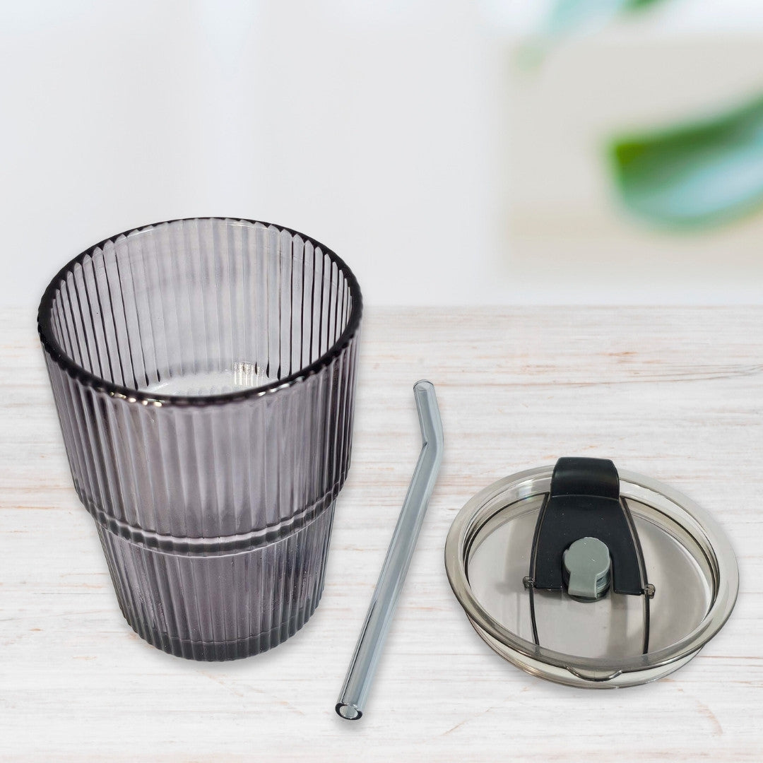 Soulistic ribbed glass sipper with a lid and straw next to it on a light marble surface