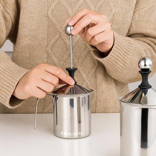 Person using a stainless steel milk frother with 'Soulistic' branding on it.